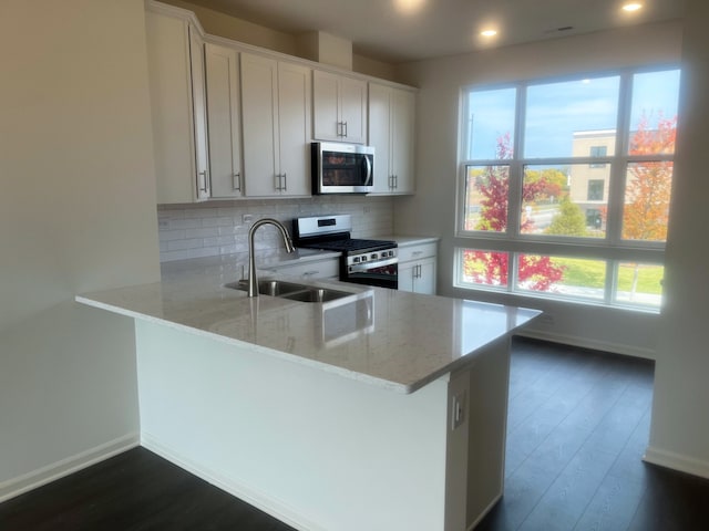 kitchen with kitchen peninsula, appliances with stainless steel finishes, light stone counters, sink, and white cabinetry