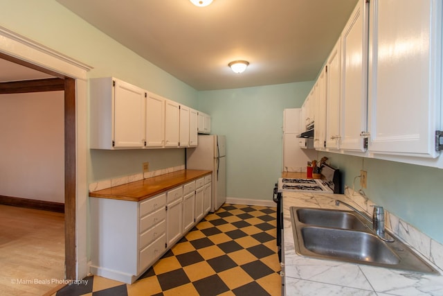 kitchen featuring sink, dark wood-type flooring, stainless steel gas range oven, white fridge, and white cabinets