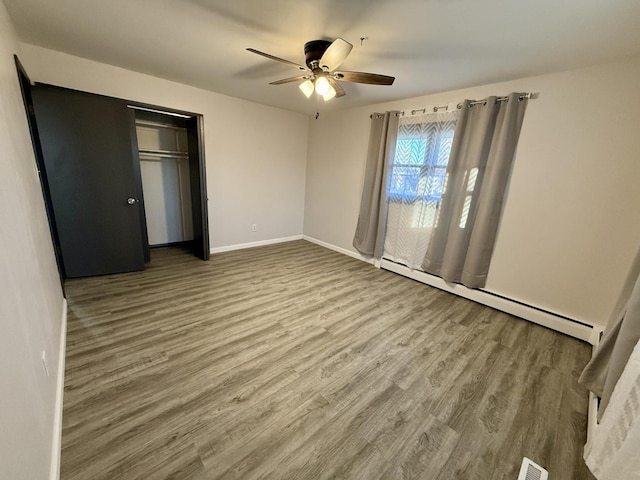 unfurnished bedroom with hardwood / wood-style flooring, ceiling fan, a closet, and a baseboard heating unit