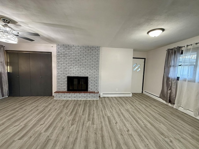 unfurnished living room featuring ceiling fan, a baseboard radiator, light hardwood / wood-style flooring, a textured ceiling, and a fireplace