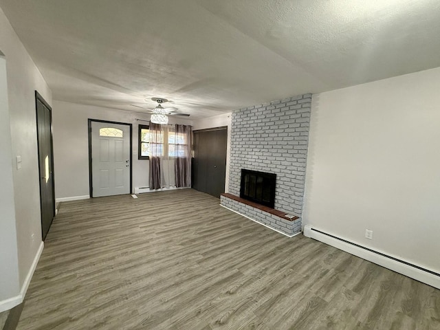 unfurnished living room with ceiling fan, a brick fireplace, a baseboard heating unit, wood-type flooring, and a textured ceiling