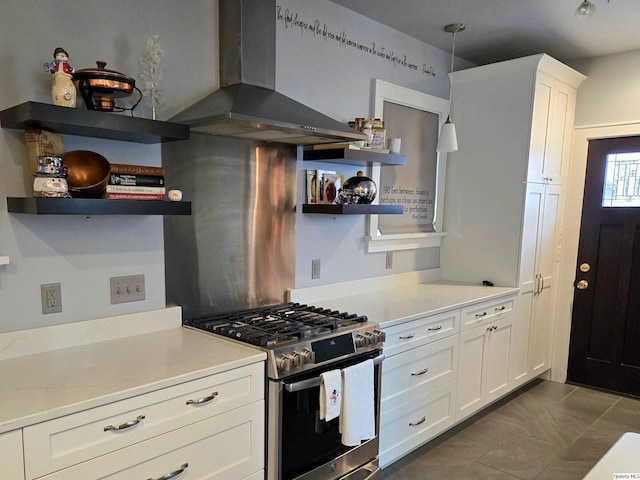 kitchen with stainless steel gas stove, wall chimney range hood, pendant lighting, and white cabinetry