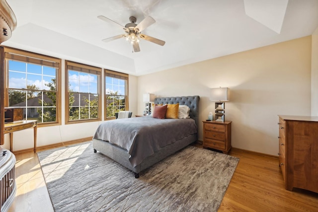 bedroom with a raised ceiling, ceiling fan, and light hardwood / wood-style floors