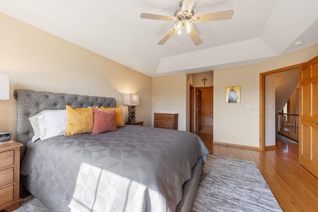 bedroom with a tray ceiling, ensuite bath, ceiling fan, and light wood-type flooring