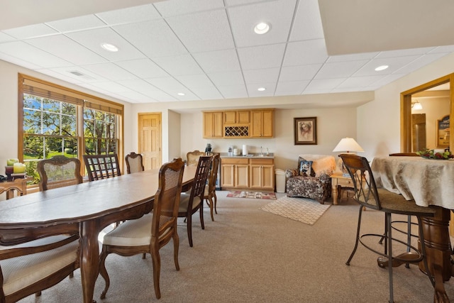 carpeted dining area featuring a drop ceiling and indoor bar