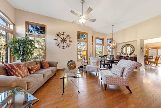 living room featuring ceiling fan with notable chandelier, light hardwood / wood-style flooring, and a towering ceiling