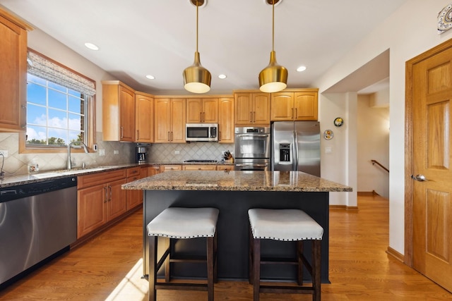 kitchen featuring stone countertops, pendant lighting, a center island, light hardwood / wood-style floors, and stainless steel appliances