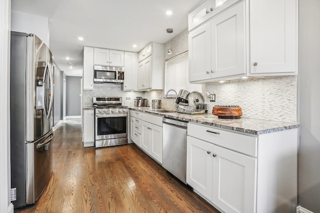 kitchen with appliances with stainless steel finishes, dark hardwood / wood-style flooring, tasteful backsplash, light stone counters, and white cabinets