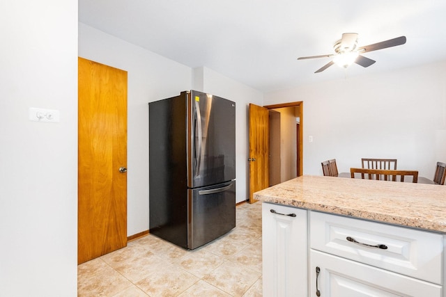 kitchen featuring white cabinets, ceiling fan, stainless steel fridge, light stone countertops, and light tile patterned flooring