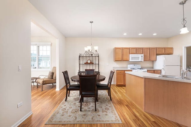 kitchen with white appliances, sink, decorative light fixtures, light hardwood / wood-style flooring, and an inviting chandelier