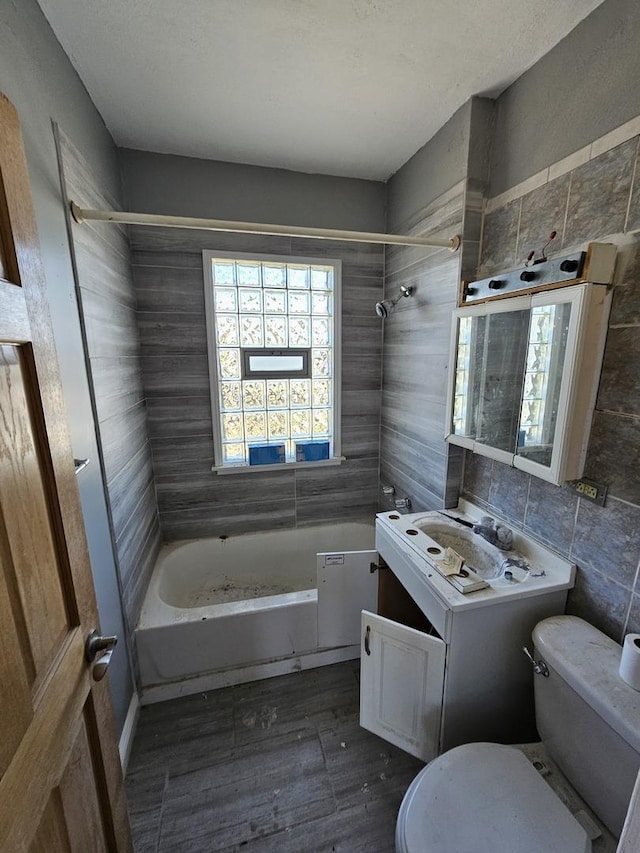 full bathroom with vanity, tiled shower / bath, hardwood / wood-style flooring, toilet, and tile walls