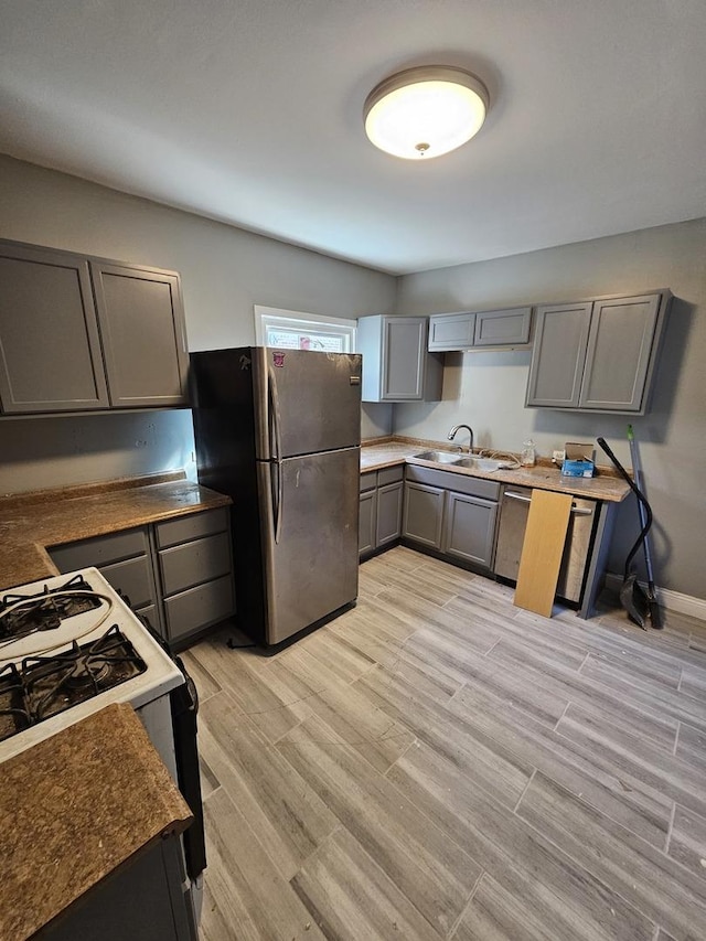 kitchen with sink, gray cabinets, stainless steel fridge, light wood-type flooring, and gas range gas stove