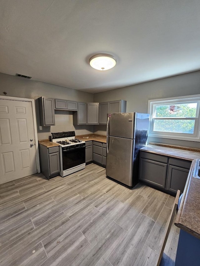 kitchen with gray cabinets, stainless steel fridge, light wood-type flooring, and white range with gas stovetop