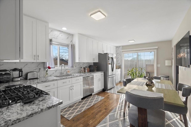 kitchen with sink, hardwood / wood-style flooring, light stone countertops, white cabinetry, and stainless steel appliances