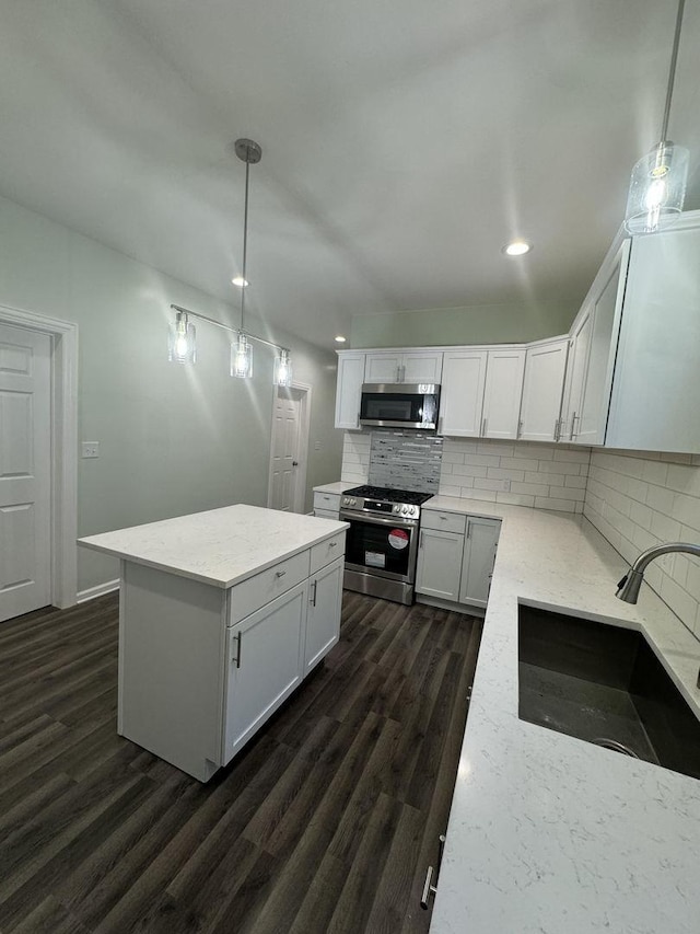 kitchen with appliances with stainless steel finishes, dark wood-type flooring, sink, white cabinets, and hanging light fixtures