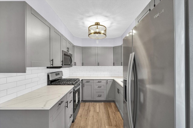 kitchen with gray cabinetry, light stone counters, stainless steel appliances, and light hardwood / wood-style flooring