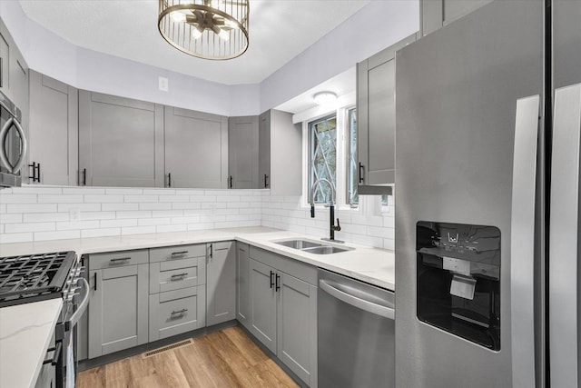 kitchen featuring decorative backsplash, appliances with stainless steel finishes, light stone countertops, sink, and light hardwood / wood-style flooring