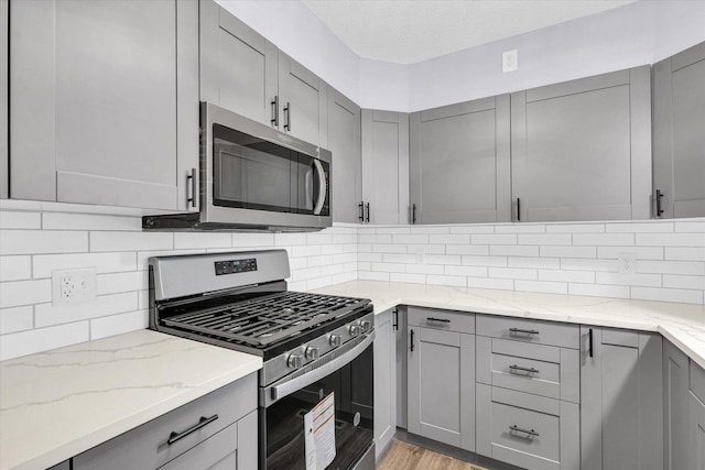 kitchen with a textured ceiling, light hardwood / wood-style floors, backsplash, and appliances with stainless steel finishes