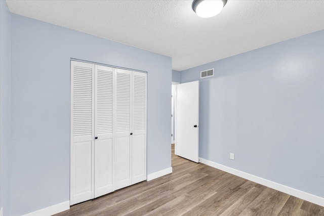 unfurnished bedroom featuring light hardwood / wood-style floors, a textured ceiling, and a closet