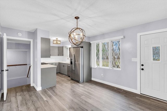 kitchen featuring gray cabinetry, stainless steel refrigerator with ice dispenser, hanging light fixtures, light wood-type flooring, and tasteful backsplash