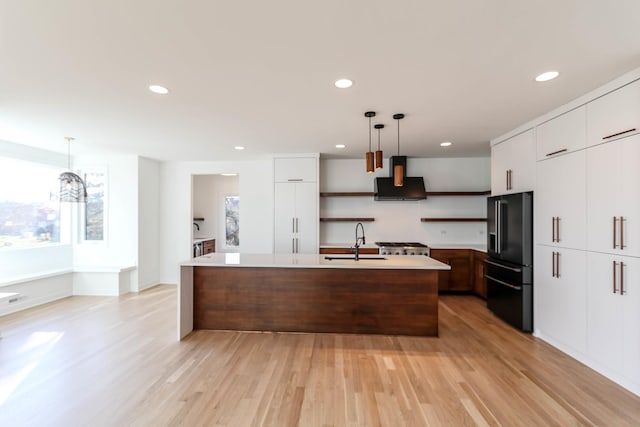 kitchen featuring black refrigerator with ice dispenser, a center island with sink, hanging light fixtures, and light hardwood / wood-style floors