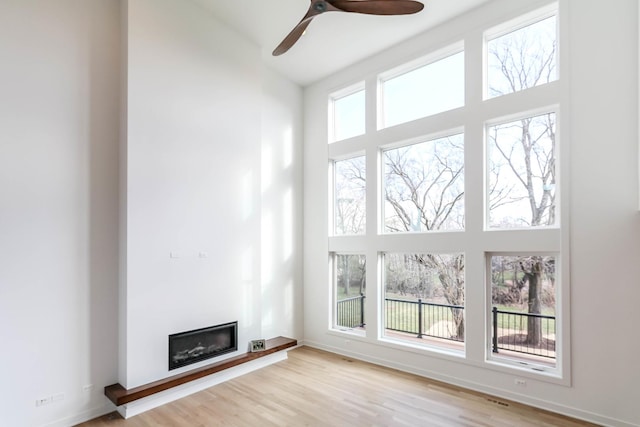 unfurnished living room featuring a high ceiling, light hardwood / wood-style flooring, plenty of natural light, and ceiling fan