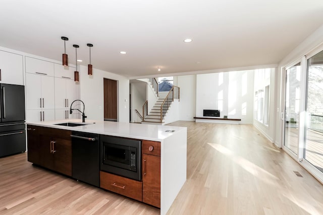 kitchen featuring sink, light hardwood / wood-style floors, decorative light fixtures, a kitchen island with sink, and black appliances