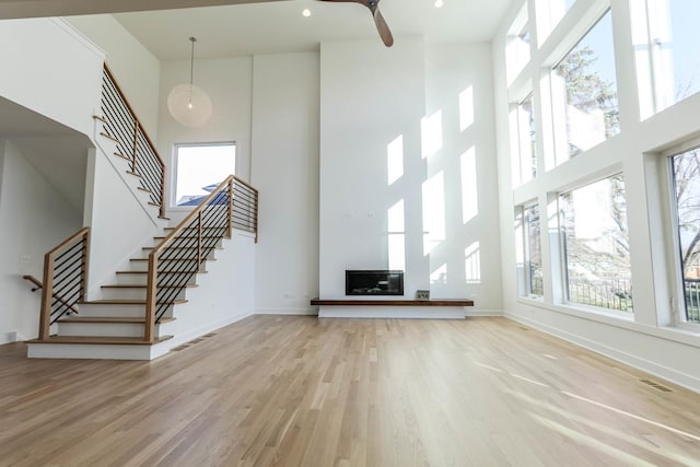 unfurnished living room featuring ceiling fan, wood-type flooring, and a towering ceiling