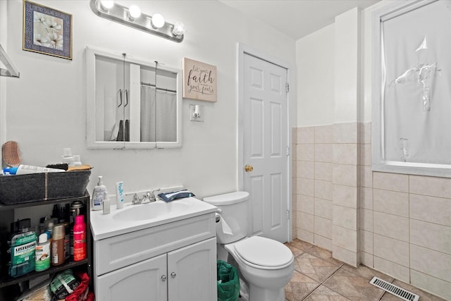 bathroom featuring tile patterned flooring, vanity, toilet, and tile walls