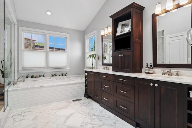 bathroom featuring a relaxing tiled tub, vanity, and vaulted ceiling