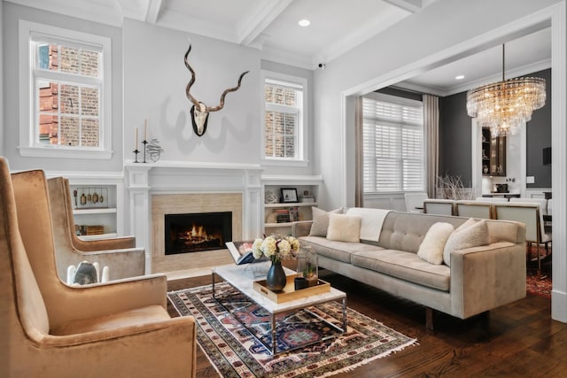 living room with crown molding, dark wood-type flooring, an inviting chandelier, a premium fireplace, and beamed ceiling