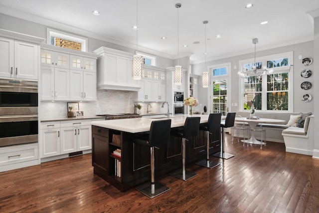 kitchen featuring white cabinets, decorative light fixtures, a kitchen island with sink, and dark wood-type flooring