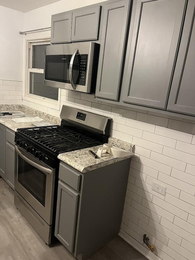 kitchen featuring gray cabinetry, decorative backsplash, appliances with stainless steel finishes, light hardwood / wood-style floors, and light stone counters