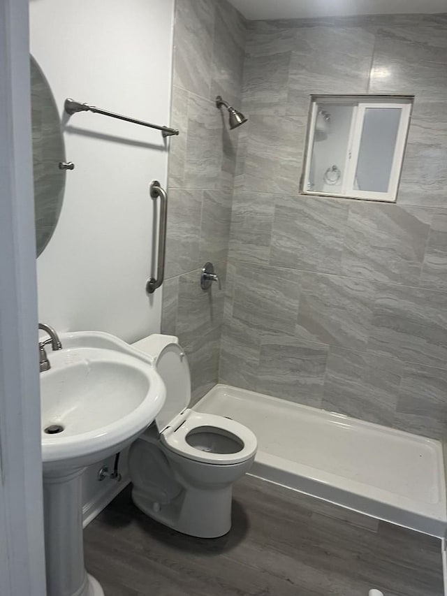 bathroom with tiled shower, hardwood / wood-style flooring, toilet, and sink