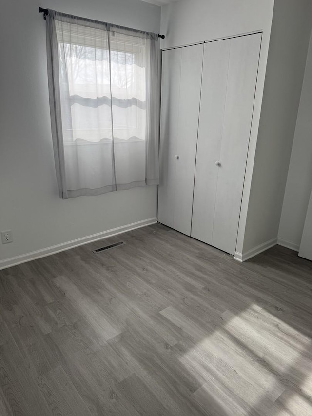 unfurnished bedroom featuring a closet, wood finished floors, visible vents, and baseboards