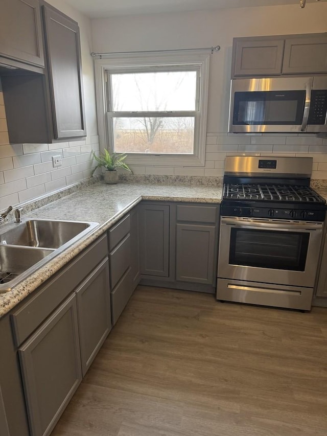 kitchen with appliances with stainless steel finishes, a sink, light wood-style floors, and gray cabinetry