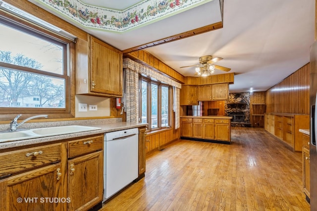 kitchen with ceiling fan, wooden walls, sink, light hardwood / wood-style flooring, and dishwasher