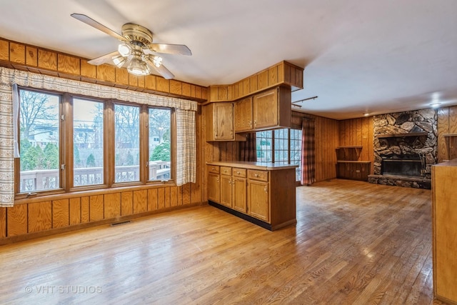 kitchen featuring kitchen peninsula, light wood-type flooring, ceiling fan, a fireplace, and wood walls