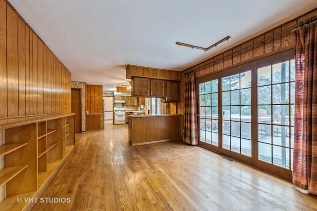 kitchen featuring kitchen peninsula, stove, light hardwood / wood-style floors, wooden walls, and white fridge