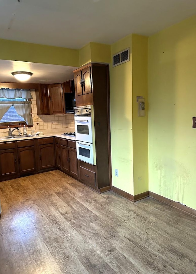 kitchen with white double oven, sink, light wood-type flooring, tasteful backsplash, and gas cooktop