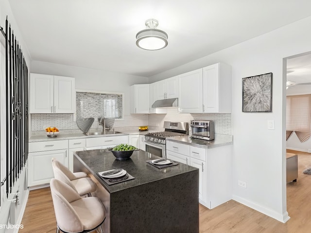 kitchen featuring a kitchen island, stainless steel range with gas cooktop, sink, and white cabinetry