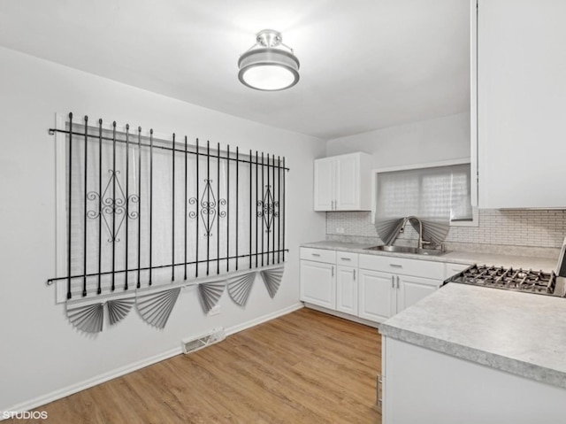 kitchen featuring decorative backsplash, white cabinetry, sink, and light hardwood / wood-style flooring