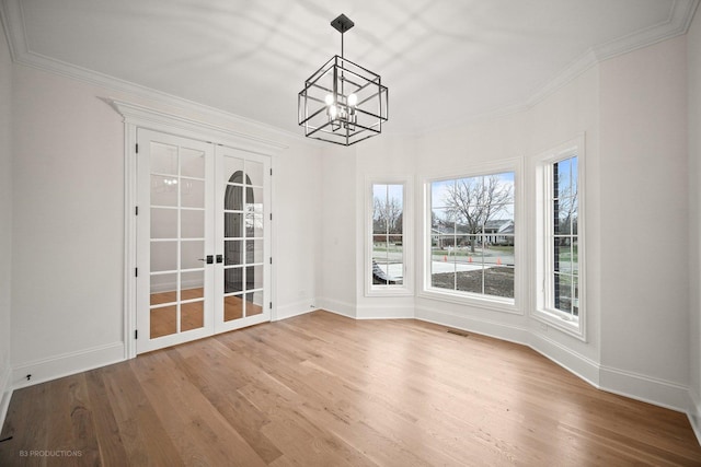 unfurnished dining area featuring french doors, an inviting chandelier, ornamental molding, and hardwood / wood-style flooring