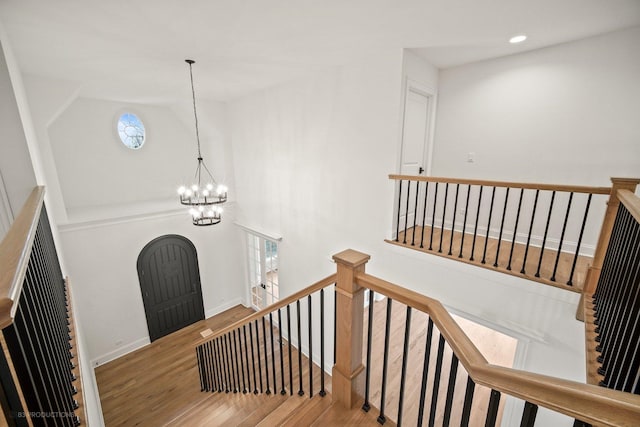 stairs featuring hardwood / wood-style floors, a chandelier, and vaulted ceiling