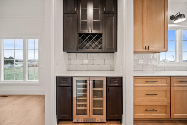 bar featuring light wood-type flooring, a wealth of natural light, beverage cooler, and backsplash