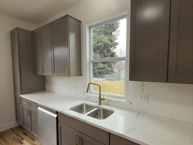 kitchen featuring light stone countertops, dishwasher, light wood-type flooring, and sink