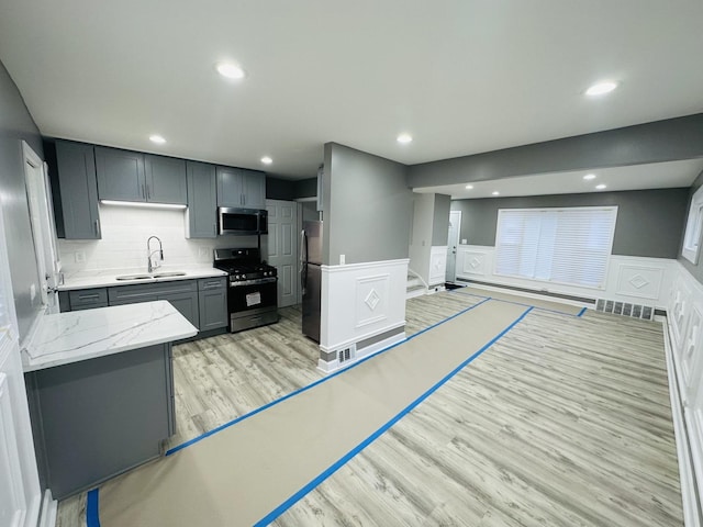 kitchen featuring appliances with stainless steel finishes, backsplash, gray cabinetry, sink, and light hardwood / wood-style floors