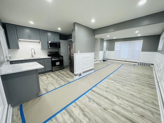 kitchen featuring gray cabinetry, sink, tasteful backsplash, light hardwood / wood-style flooring, and appliances with stainless steel finishes