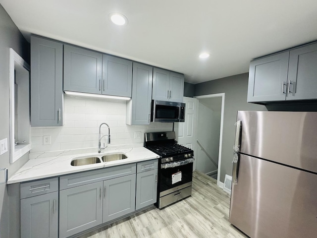 kitchen with gray cabinetry, sink, decorative backsplash, appliances with stainless steel finishes, and light wood-type flooring