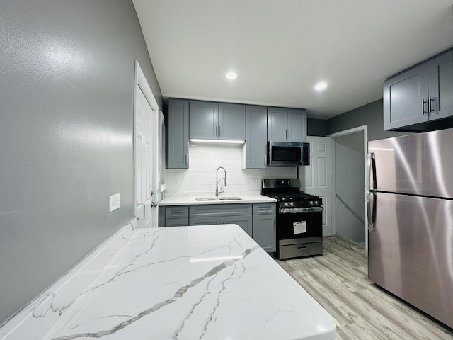 kitchen with gray cabinetry, sink, appliances with stainless steel finishes, light hardwood / wood-style floors, and light stone counters